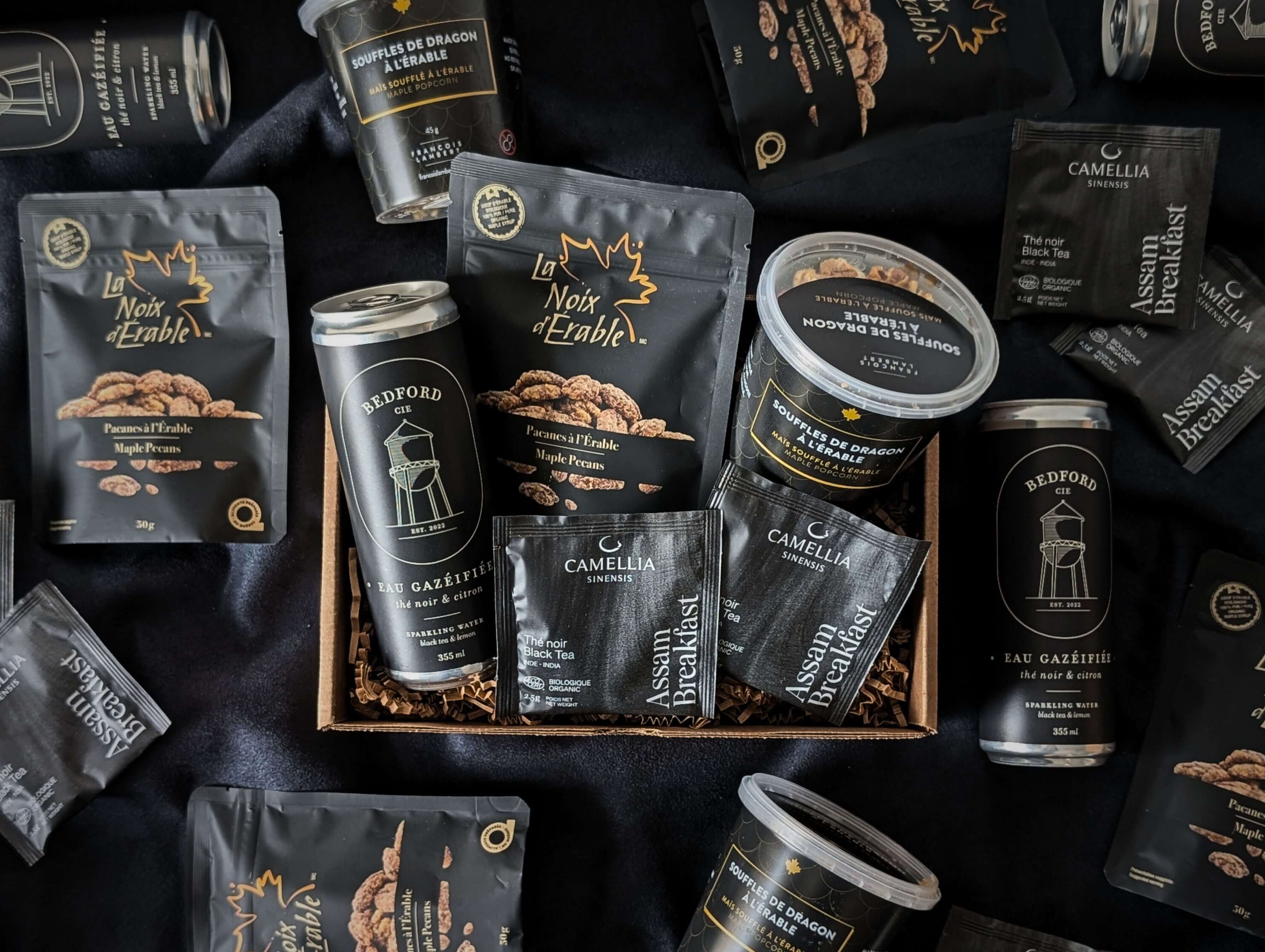 Boîte Noir gourmand avec pacanes à l’érable, eau pétillante thé noir et collations locales sucrées salées